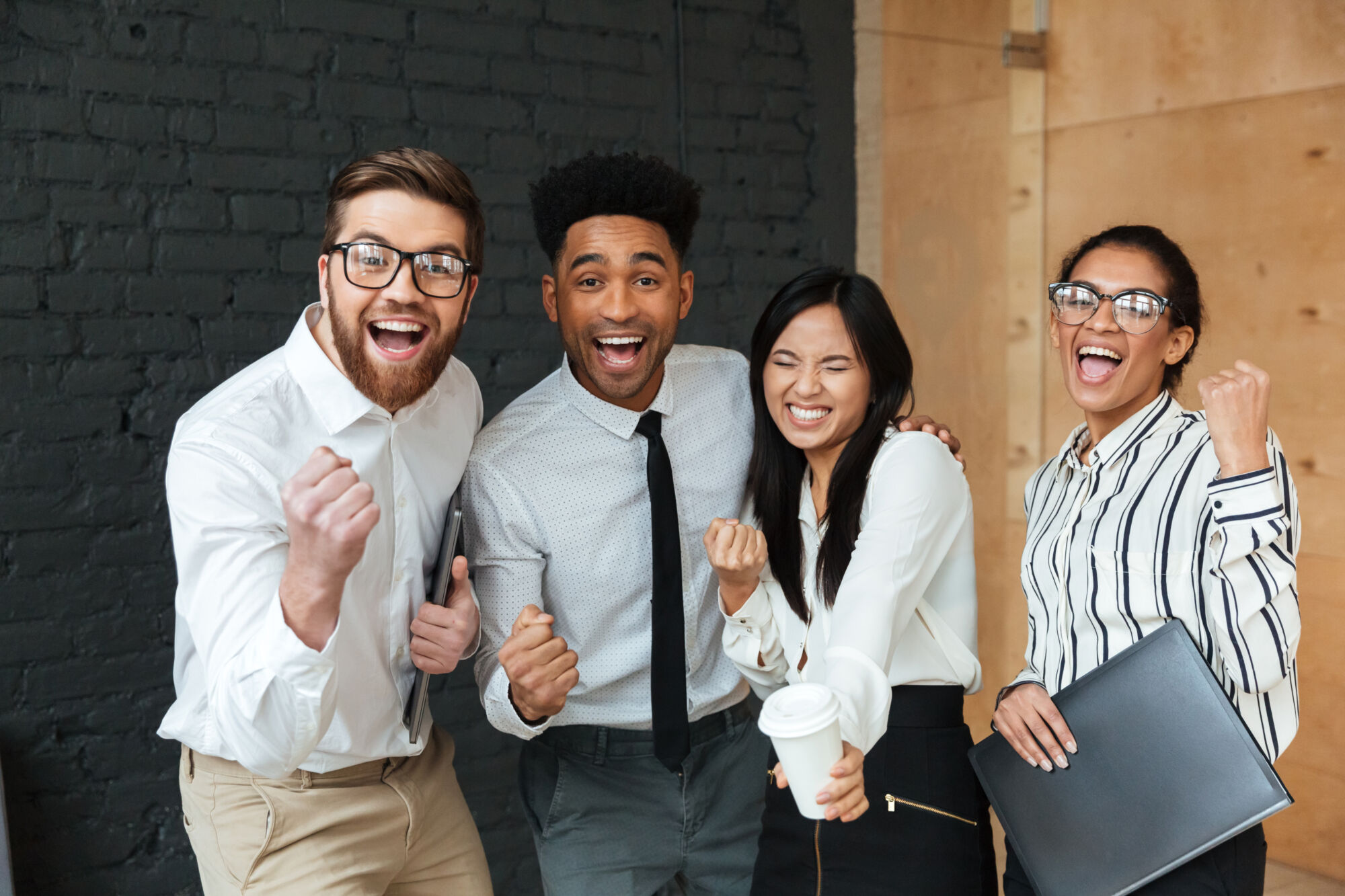 Photo of happy excited young business colleagues indoors coworking. Looking camera make winner gesture.